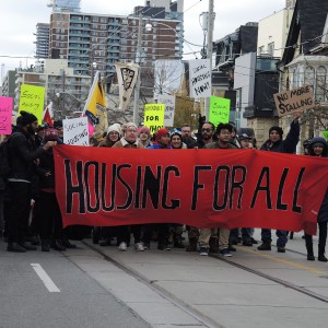 Ani-poverty activists marching in Toronto holding colourful banners, including a large red banner that says