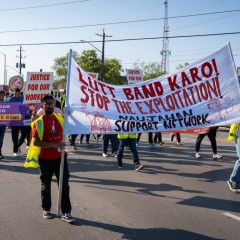 A photo of people marching on a road in Brampton. Two people in the front are carrying a large banner that says