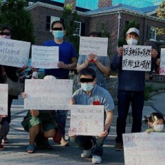 A group of Asian community members wearing masks and holding up signs in multiple languages with anti-trafficking messages written on them.