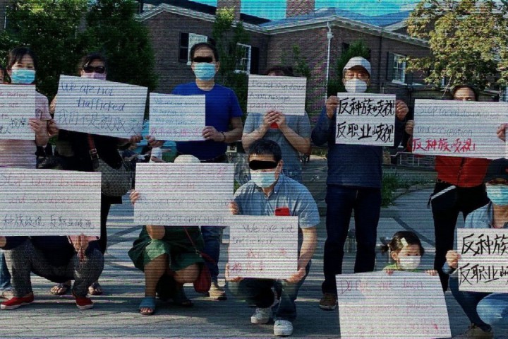 A group of Asian community members wearing masks and holding up signs in multiple languages with anti-trafficking messages written on them.