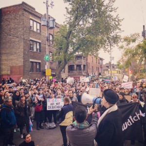 A photography of a crowd from above, listening to someone speak through a megaphone. One member of the crowd holds a sign that says