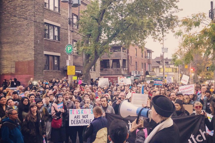 A photography of a crowd from above, listening to someone speak through a megaphone. One member of the crowd holds a sign that says