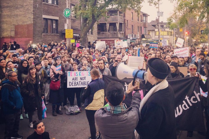 A photography of a crowd from above, listening to someone speak through a megaphone. One member of the crowd holds a sign that says